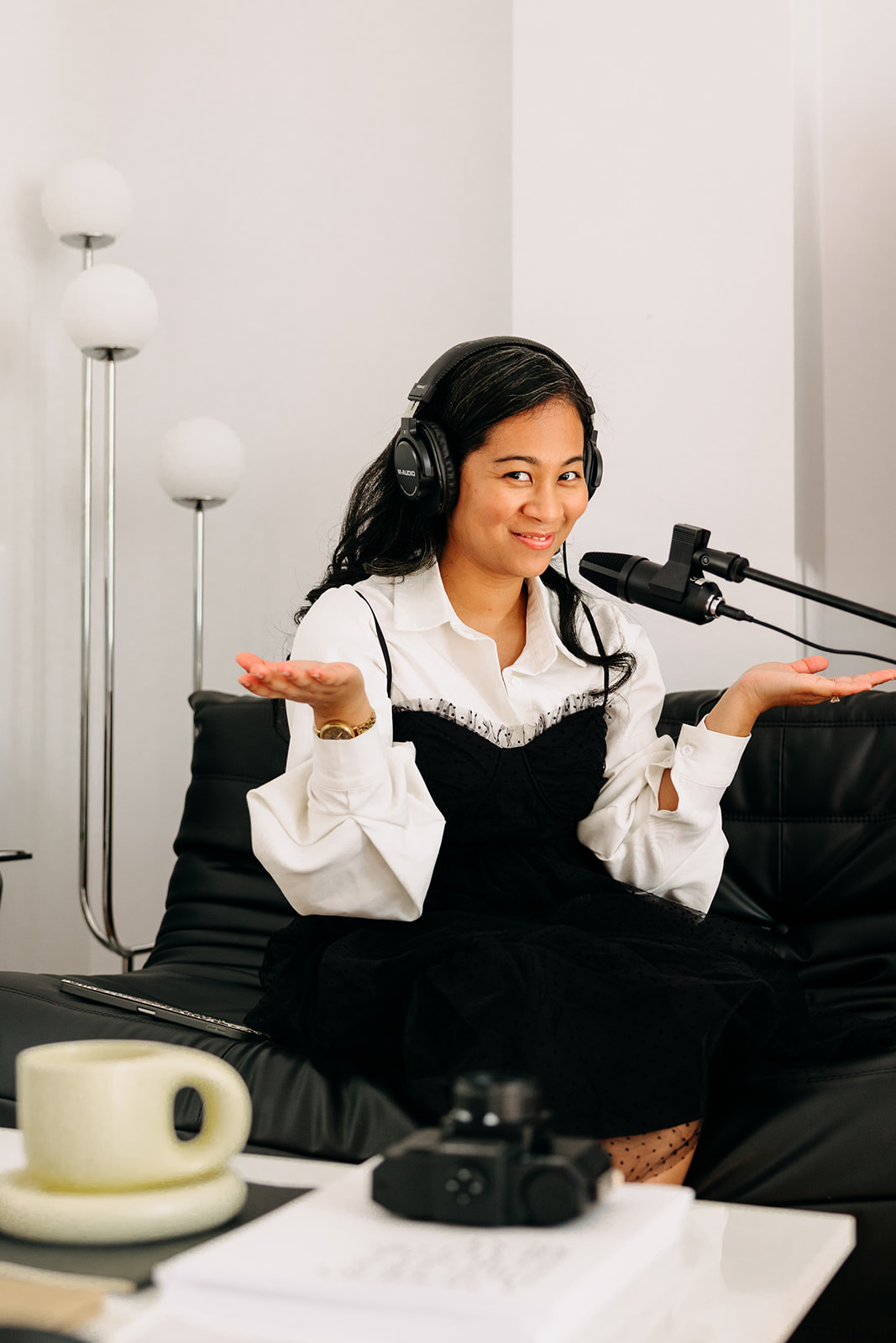 A woman dressed in black an white attire with a podcast mic and headphone smiling at the camera as she speaks about wedding photography pricing